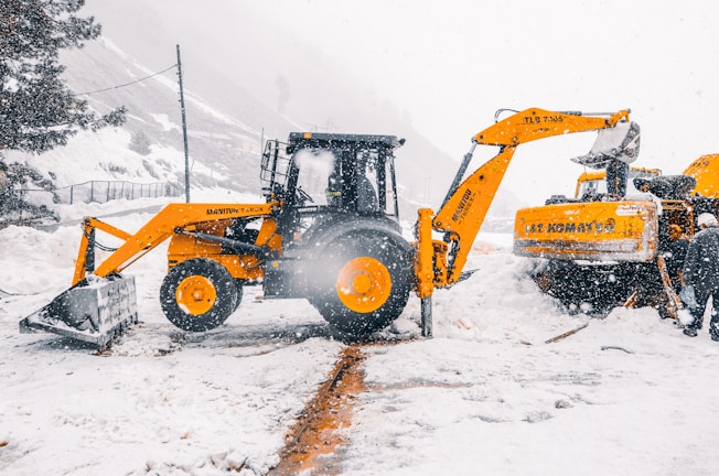 Snow being cleared and loaded onto a truck by heavy machinery on a winter day.