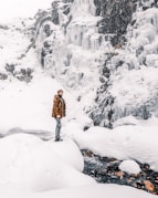 men in brown coat standing on snow covered ground