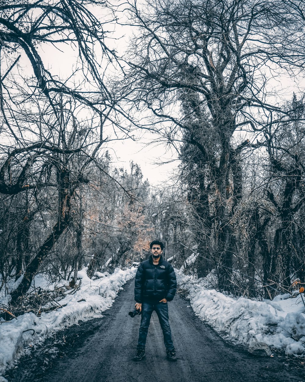 person in black jacket standing on snow covered ground near bare trees during daytime