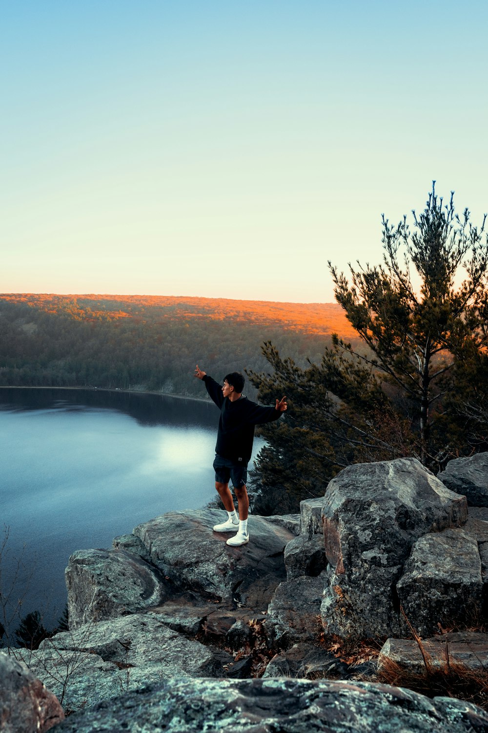 man in black jacket standing on gray rock near body of water during daytime