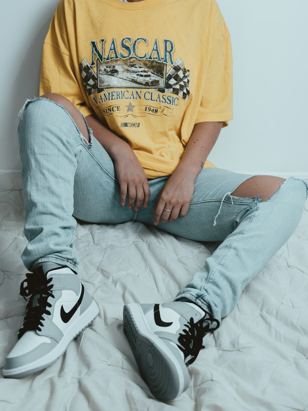man in yellow crew neck t-shirt and gray denim jeans sitting on white bed
