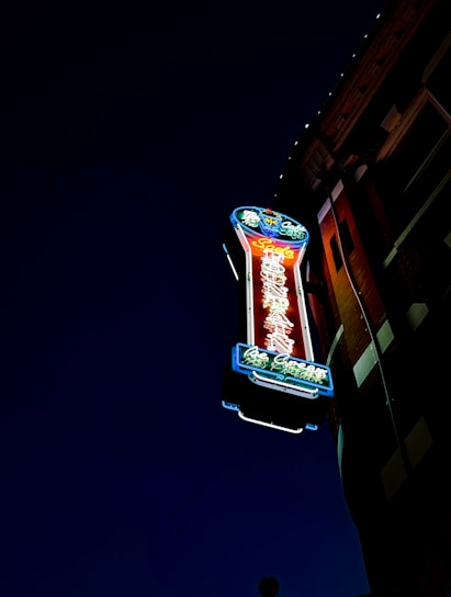 A skilled technician installing a vibrant red and white illuminated sign on a storefront at sunset.