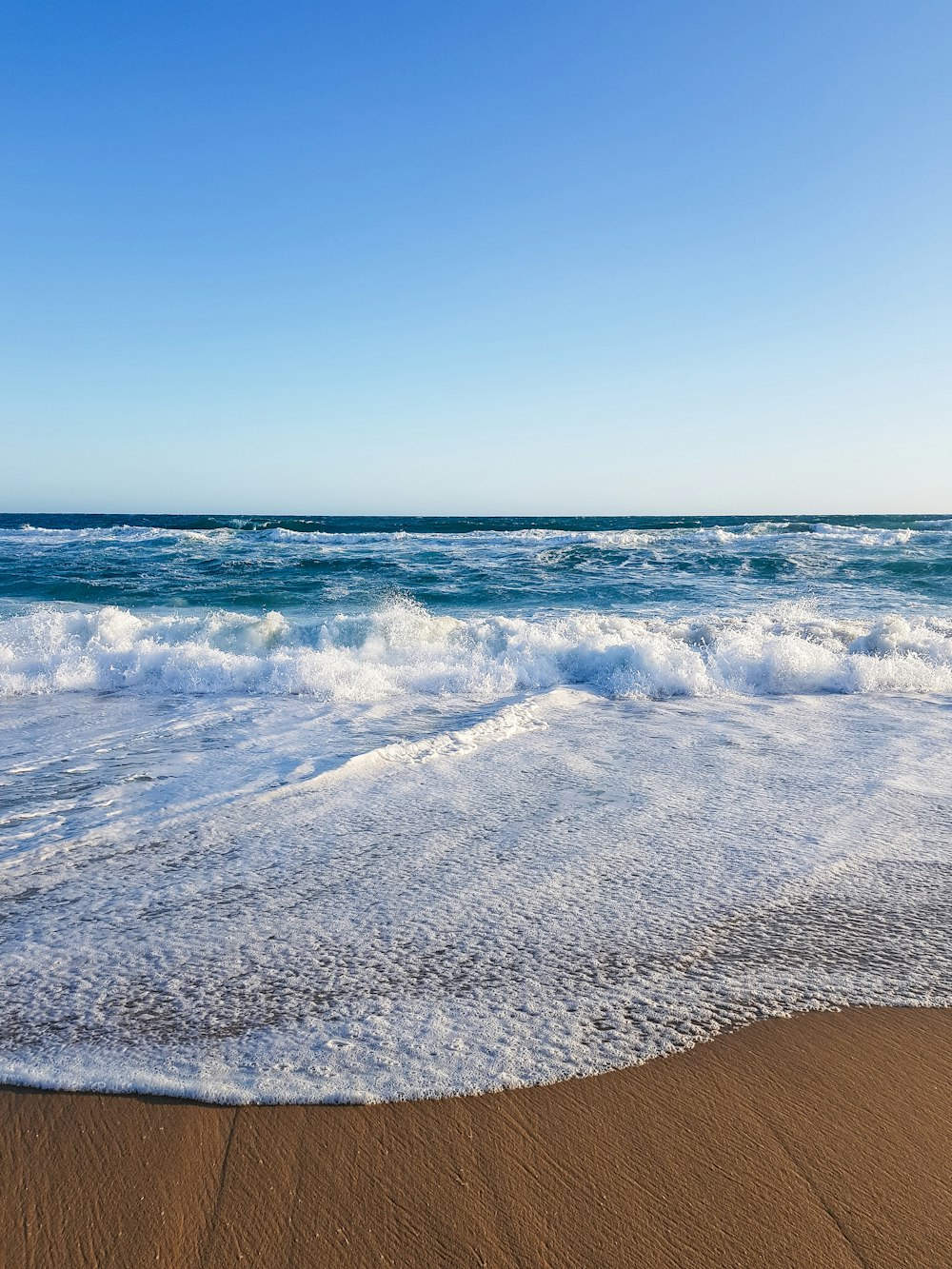 uma praia de areia com ondas que chegam à costa