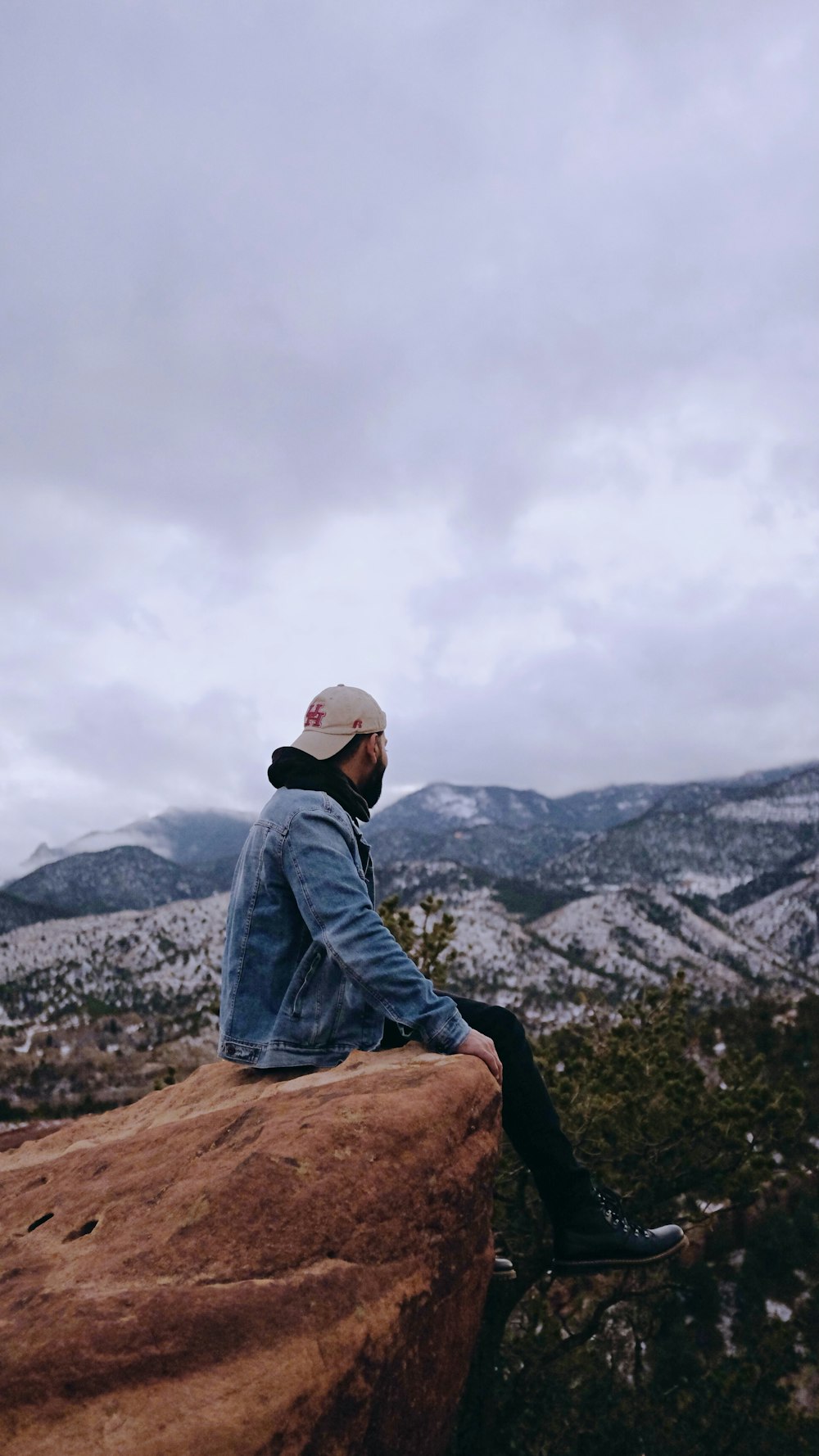 man in blue denim jacket sitting on brown rock during daytime