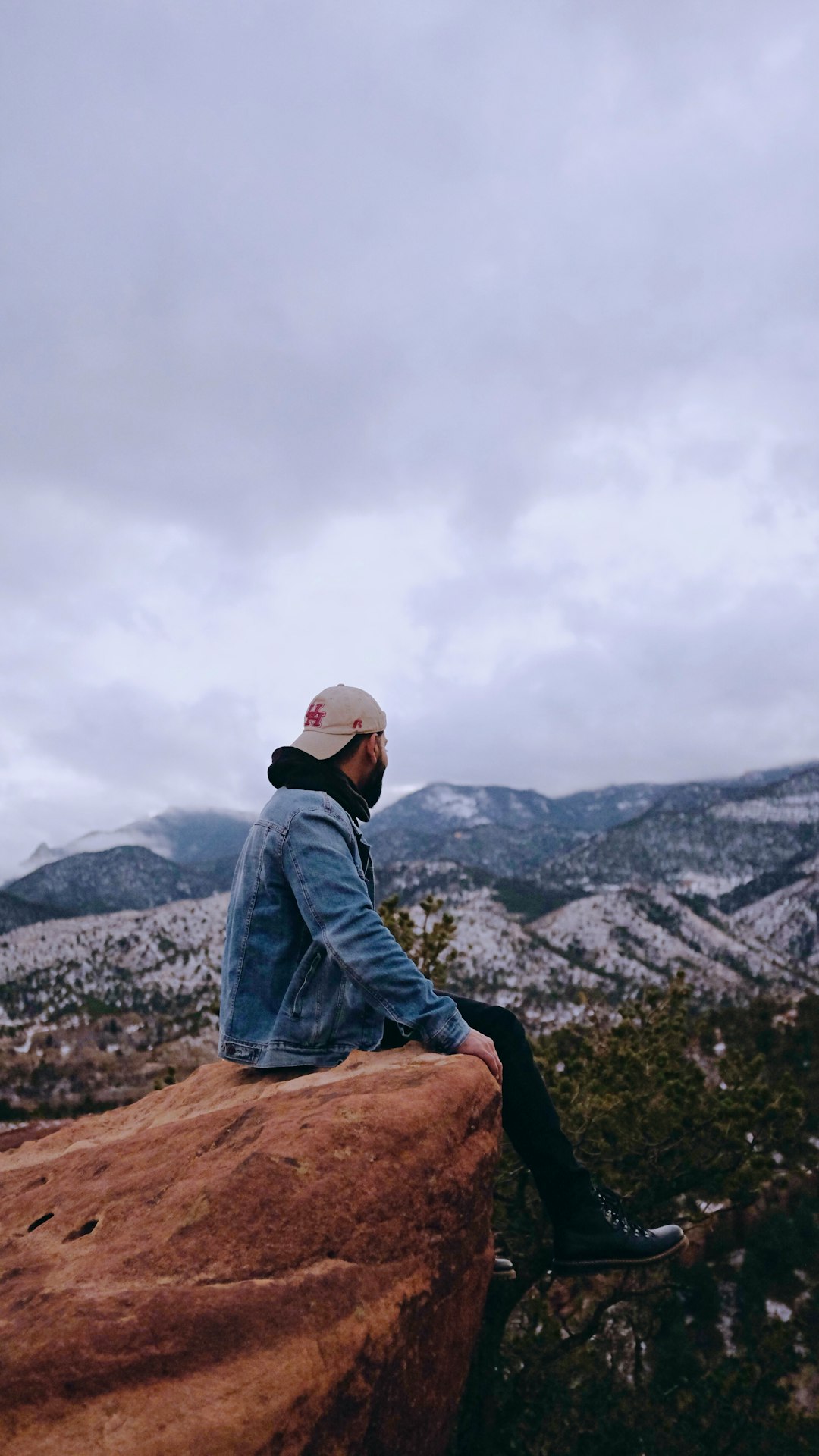 man in blue denim jacket sitting on brown rock during daytime