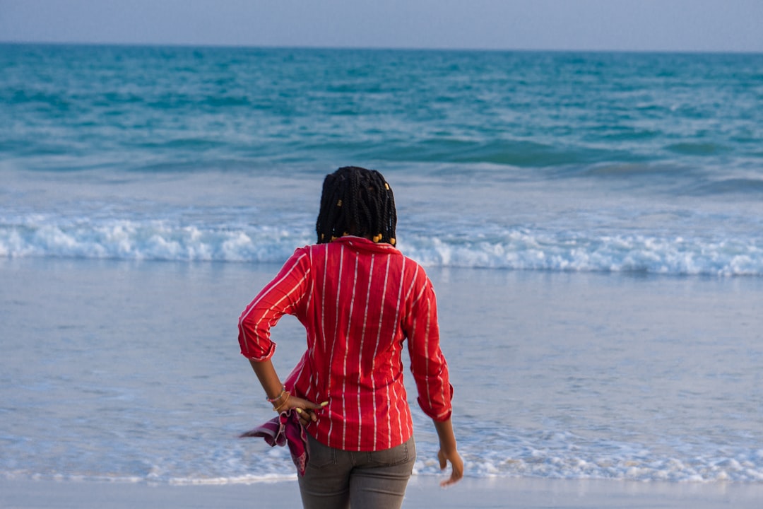 woman in red long sleeve shirt and brown skirt standing on seashore during daytime