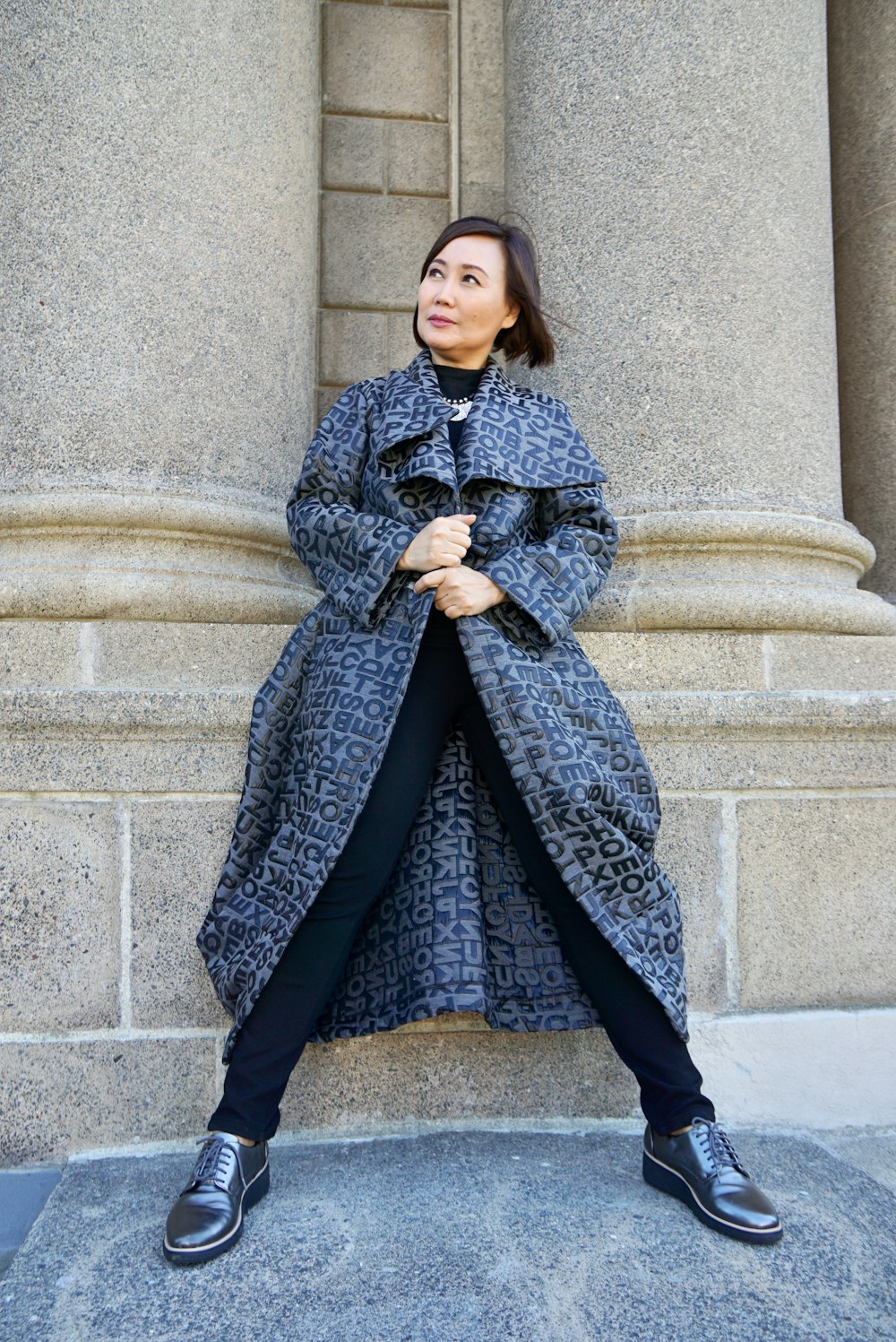 woman in gray coat standing beside gray concrete wall