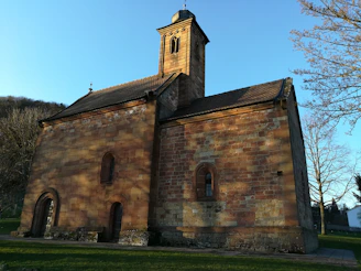 A sunlit view of Bramham Sanctum's ancient stone church tower framed by leafy branches.