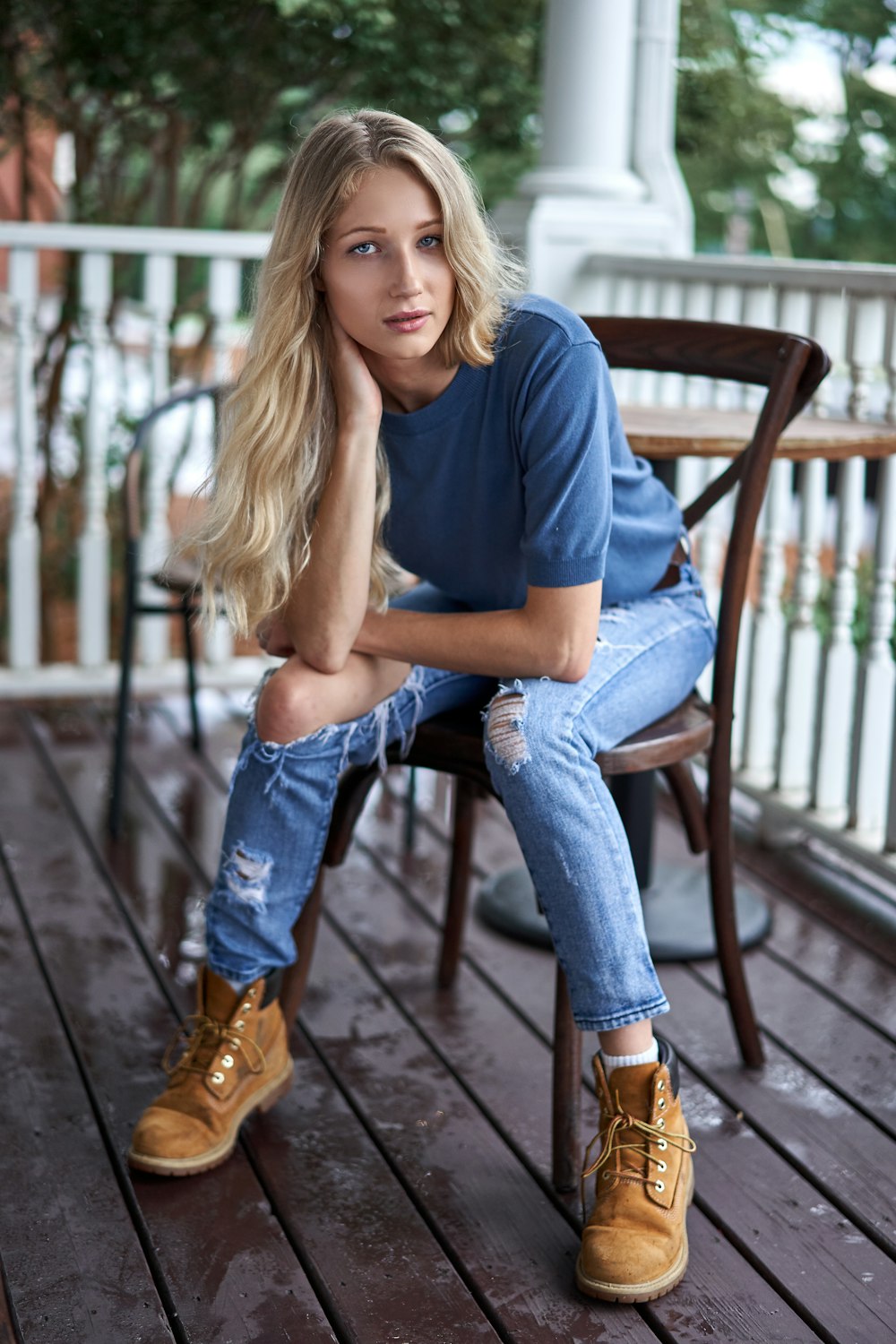 woman in blue long sleeve shirt and blue denim jeans sitting on brown wooden chair