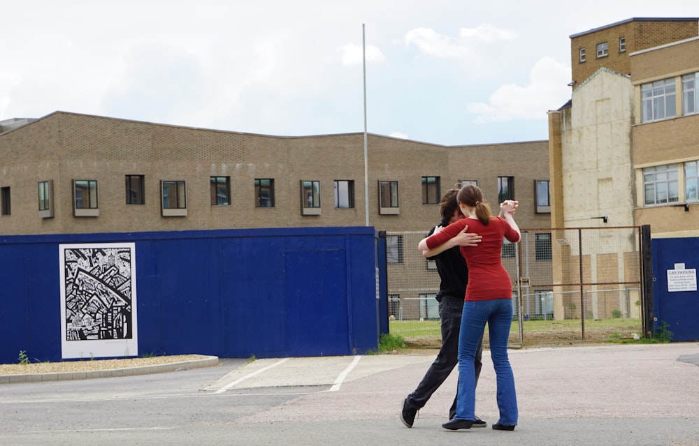 woman in red shirt and blue denim jeans standing on gray concrete floor during daytime