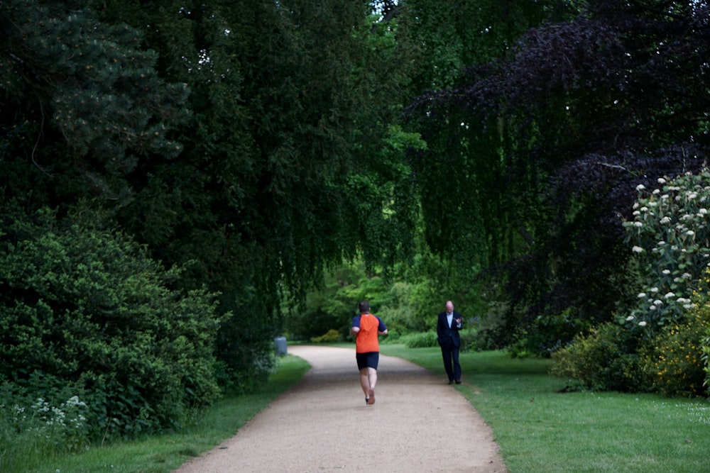2 women walking on pathway between green trees during daytime