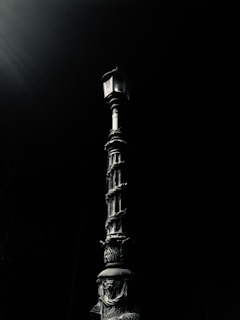 A vintage-style street lamp with ornate details stands against a dark background, its design featuring intricate patterns and curves. The lighting highlights the metallic texture of the lamp post.