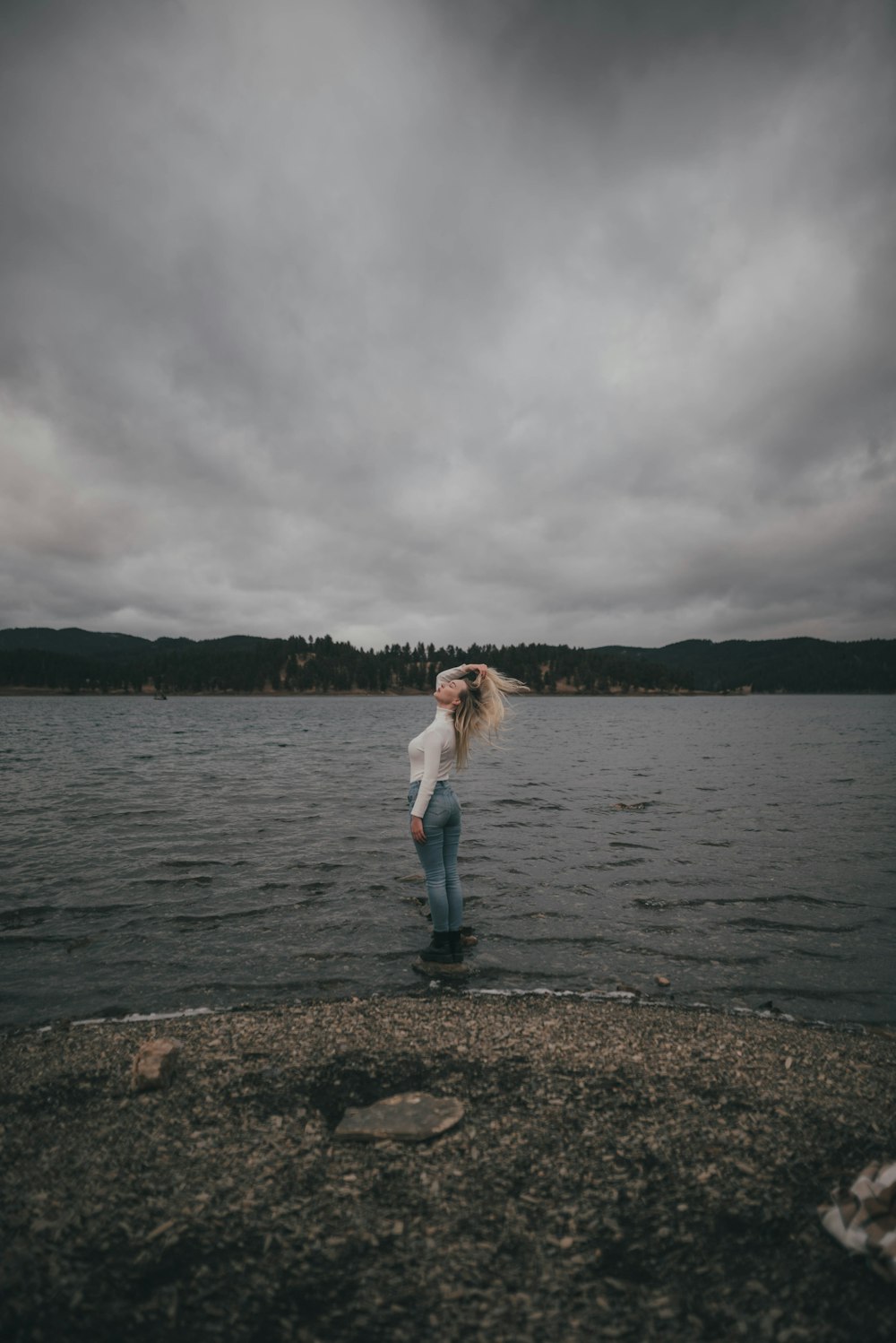 woman in white long sleeve shirt and blue denim jeans standing on brown sand near body