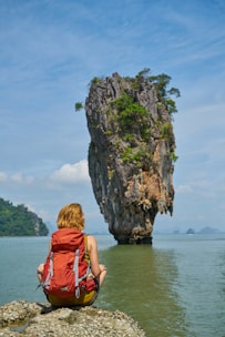 woman in red dress sitting on rock formation near body of water during daytime