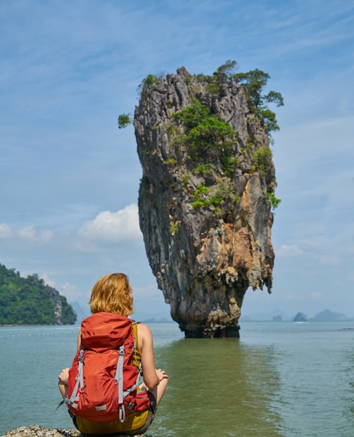 woman in red dress sitting on rock formation near body of water during daytime