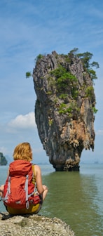 woman in red dress sitting on rock formation near body of water during daytime