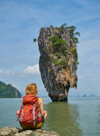 woman in red dress sitting on rock formation near body of water during daytime