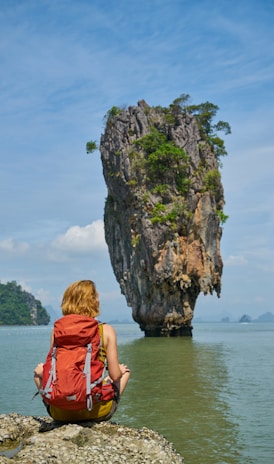 woman in red dress sitting on rock formation near body of water during daytime