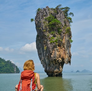 woman in red dress sitting on rock formation near body of water during daytime