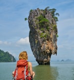 woman in red dress sitting on rock formation near body of water during daytime