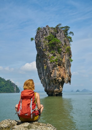 woman in red dress sitting on rock formation near body of water during daytime