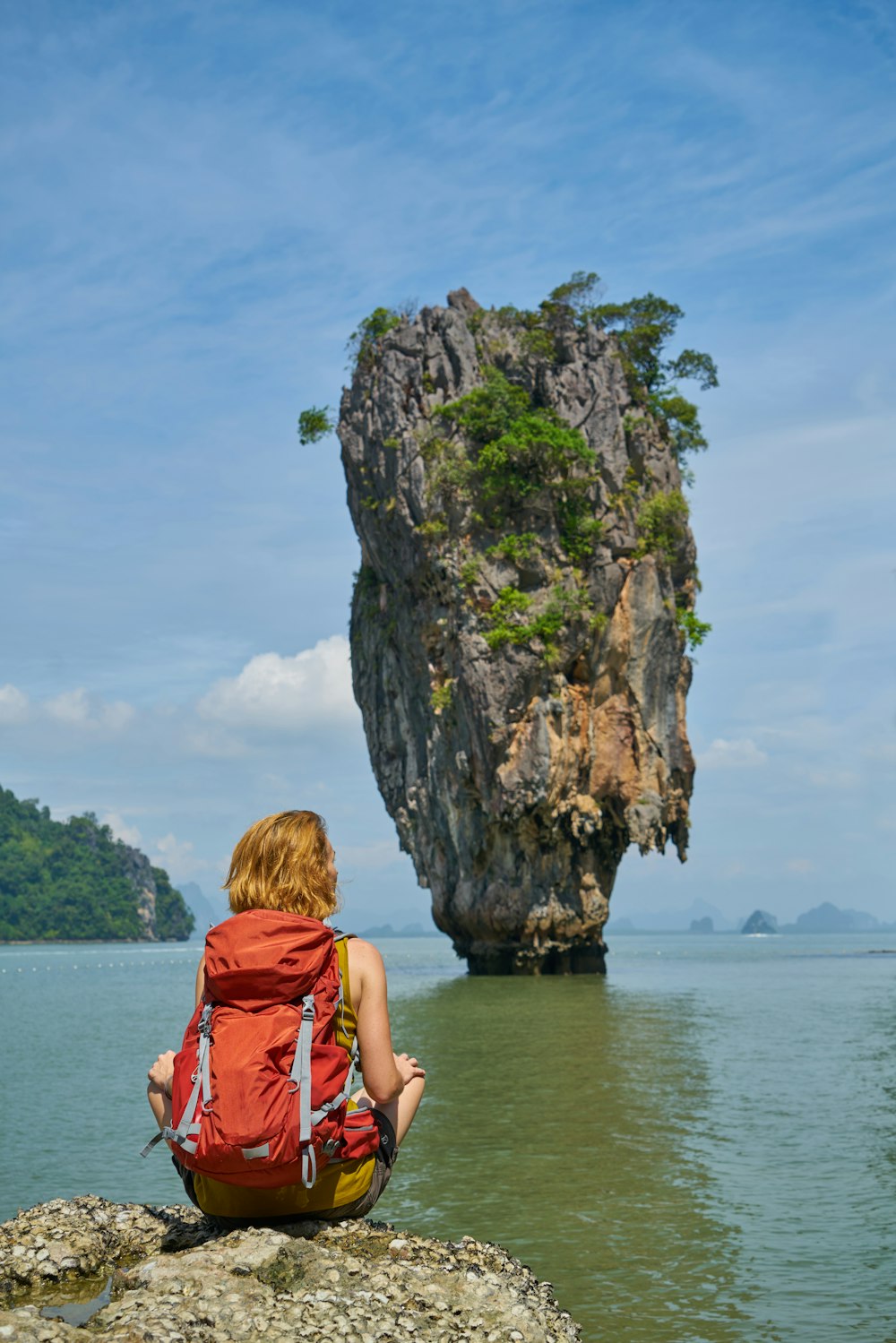 woman in red dress sitting on rock formation near body of water during daytime