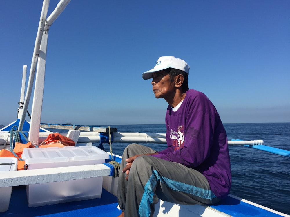 man in purple hoodie and gray pants sitting on boat during daytime