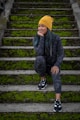 boy in black jacket and yellow knit cap sitting on concrete stairs