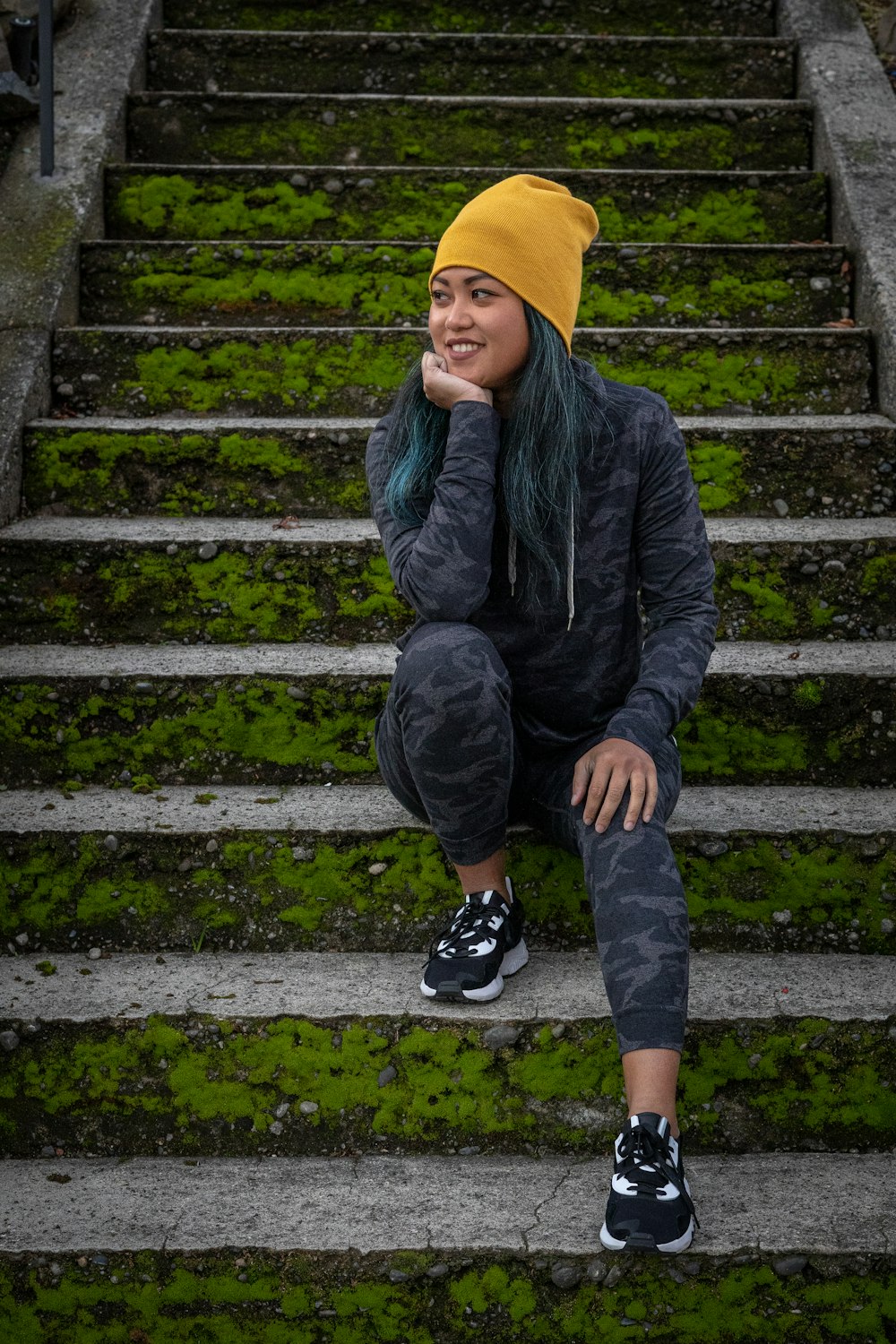 garçon en veste noire et bonnet en tricot jaune assis sur des escaliers en béton