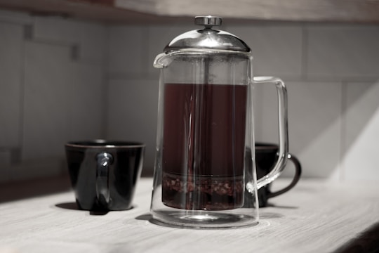 A glass French press filled with rich coffee surrounded by warm morning light.
