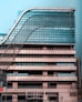 A modern multi-story office building with a distinctive wavy architectural design. The facade is made predominantly of glass and metal, with an array of vertical and horizontal lines creating a grid-like pattern. There are signs for 'National Insurance' and 'Parking 24x7' visible in multiple languages. The structure appears robust and industrial.