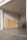 A stack of cardboard boxes is neatly arranged on pallets in a warehouse or storage area. The space is well-lit with overhead fluorescent lights, and there's a metal ladder leaning against the wall. The floor is concrete, and large double doors are partially visible.