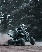 An ATV kicking up dust on a rugged trail surrounded by pine trees.