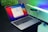 A sleek laptop with a colorful screen displaying a language selection window. The device sits on a dark surface against a contrasting backdrop of vivid lights and softly focused greenery, creating a modern and high-tech atmosphere.