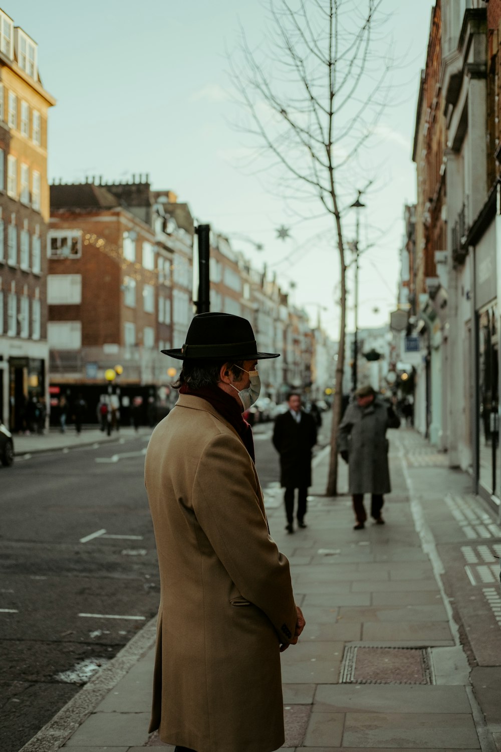 man in brown coat and black hat walking on sidewalk during daytime