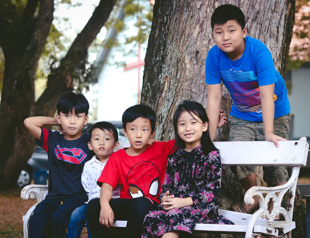 a group of children sitting on a white bench next to a tree