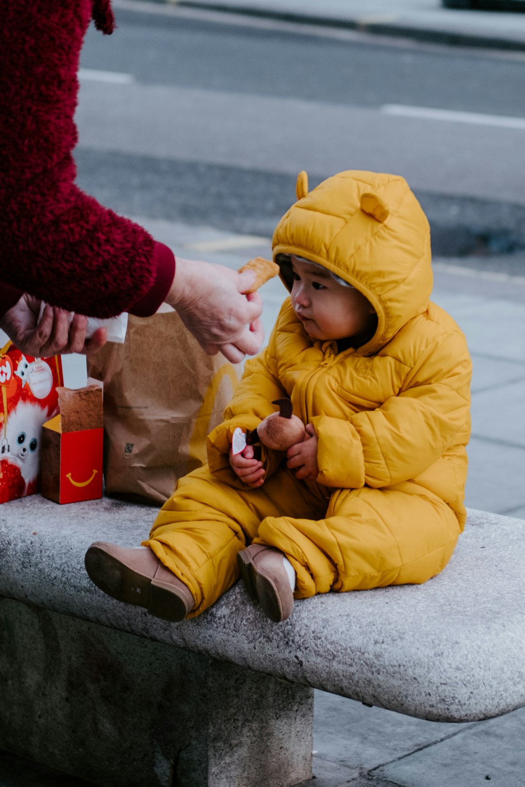 child in yellow jacket and yellow pants sitting on gray concrete floor