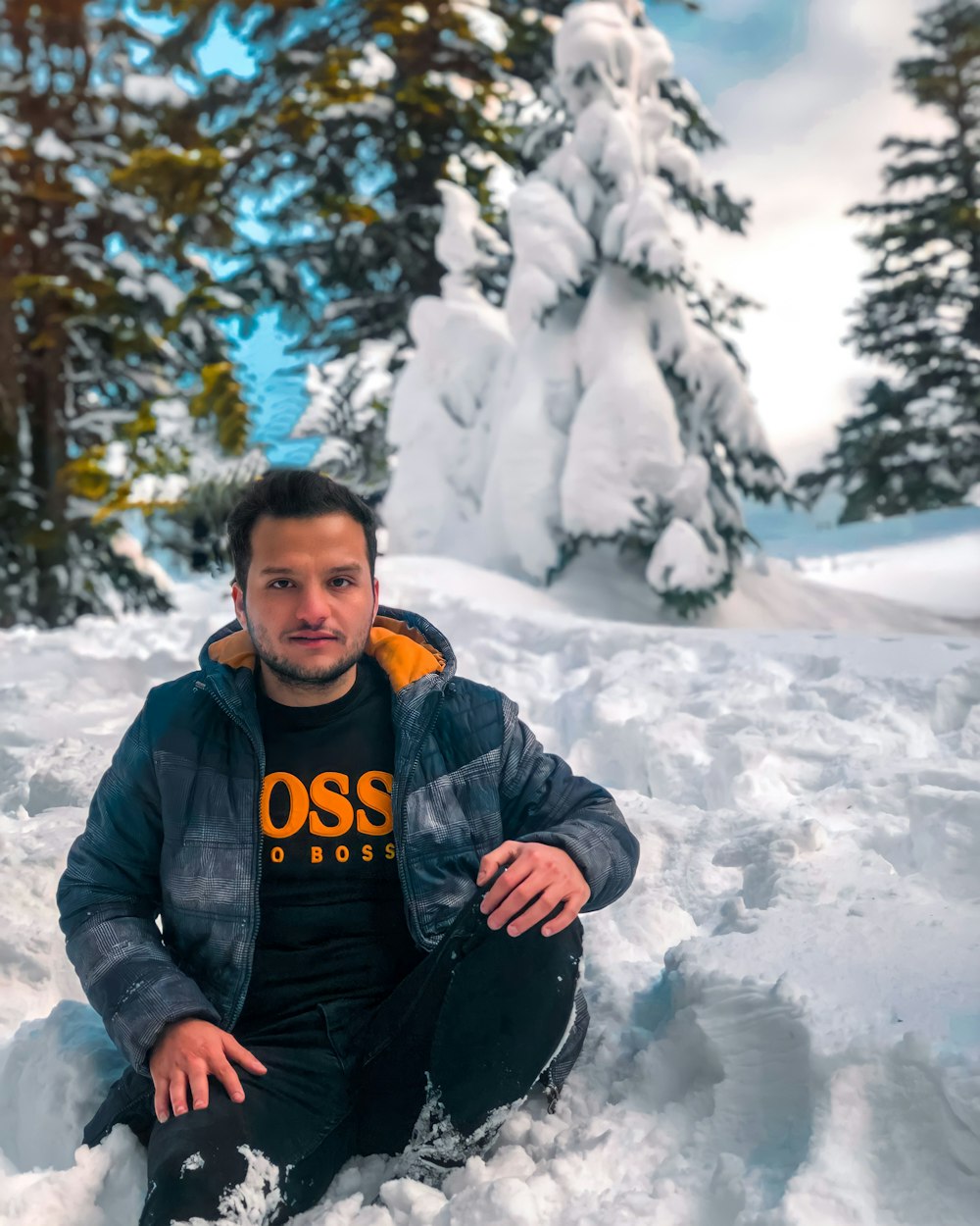 man in black jacket sitting on snow covered ground