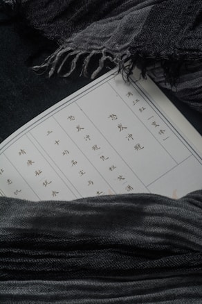 A page with Chinese characters is partially visible, surrounded by soft, dark gray fabric. The material has a textured, woven appearance and appears to envelope the page, creating an intimate, cozy setting.