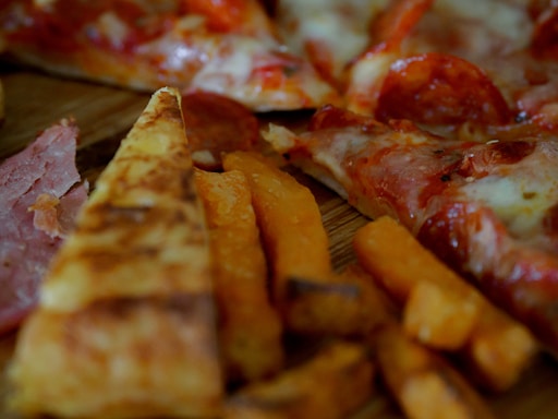 Slices of pizza with pepperoni and melted cheese are visible alongside crispy sweet potato fries. The thin crust pizza features a generous serving of toppings, including pepperoni and ham.