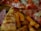 Slices of pizza with pepperoni and melted cheese are visible alongside crispy sweet potato fries. The thin crust pizza features a generous serving of toppings, including pepperoni and ham.