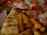 Slices of pizza with pepperoni and melted cheese are visible alongside crispy sweet potato fries. The thin crust pizza features a generous serving of toppings, including pepperoni and ham.