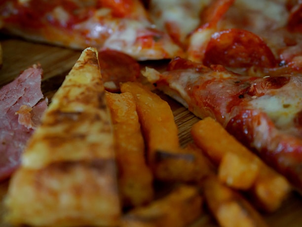 Slices of pizza with pepperoni and melted cheese are visible alongside crispy sweet potato fries. The thin crust pizza features a generous serving of toppings, including pepperoni and ham.