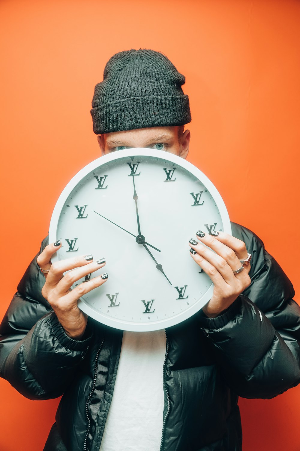 man in black knit cap and black knit cap holding white analog wall clock