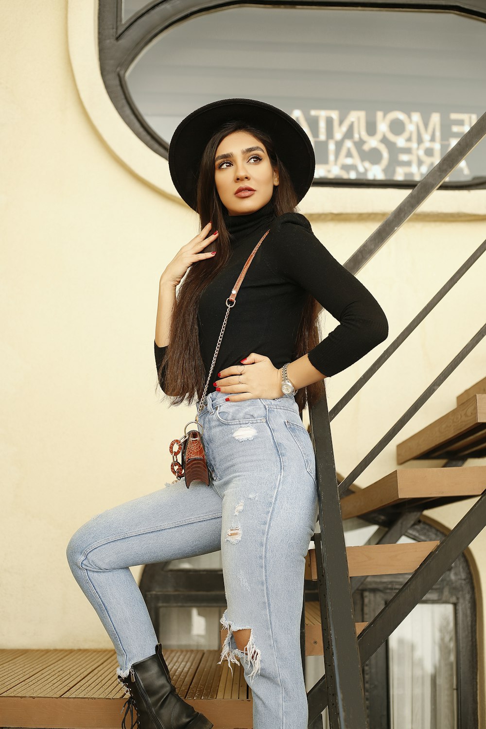 woman in black long sleeve shirt and blue denim jeans sitting on brown wooden stairs