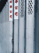 A series of metallic folding shutters form a repetitive pattern. Chinese characters in red are prominently displayed on white signs attached to the doors.