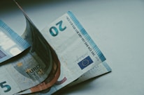 Several Euro banknotes in denominations of five and twenty are partially visible, placed on a plain surface. The focus is on the text and numbers on the banknotes, with the European Union flag and the number 20 prominently displayed.