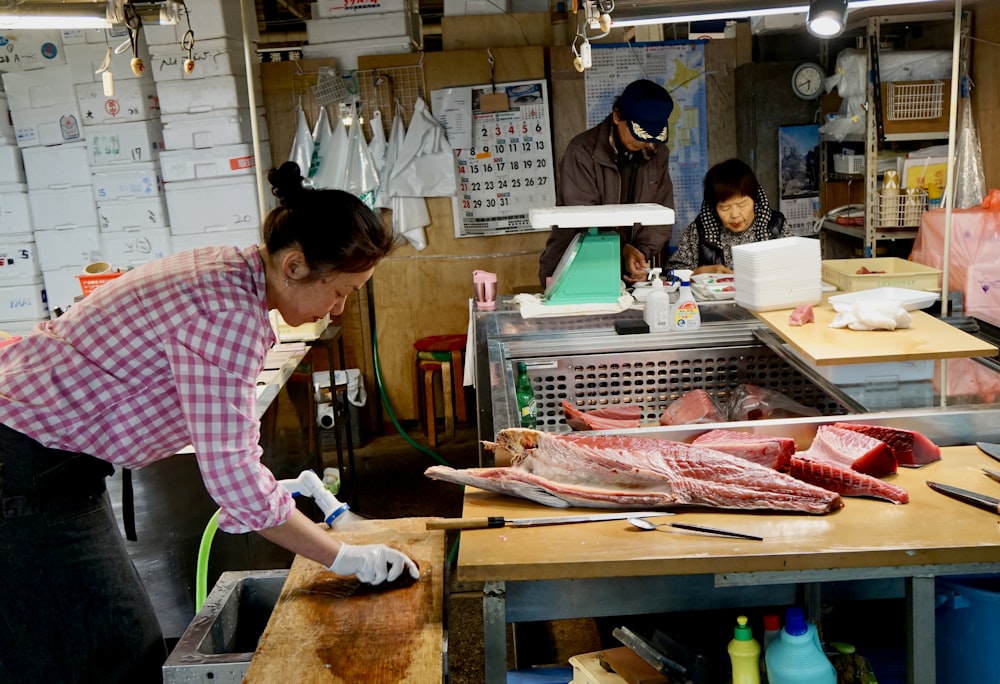 woman in pink and white long sleeve shirt slicing fish