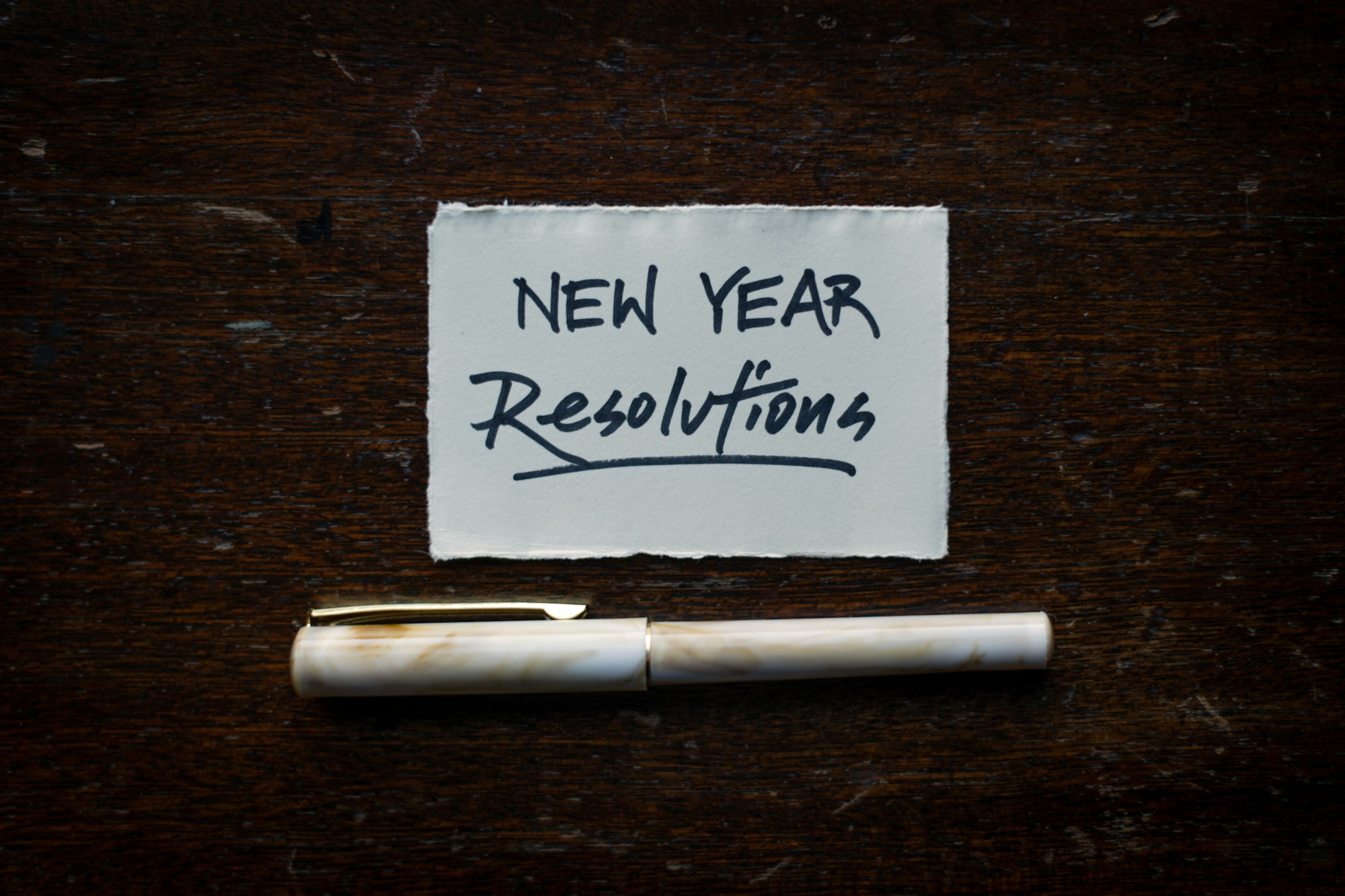 Imagen con un bolígrafo y un recorte de papel con las palabras "New Year Resolutions"