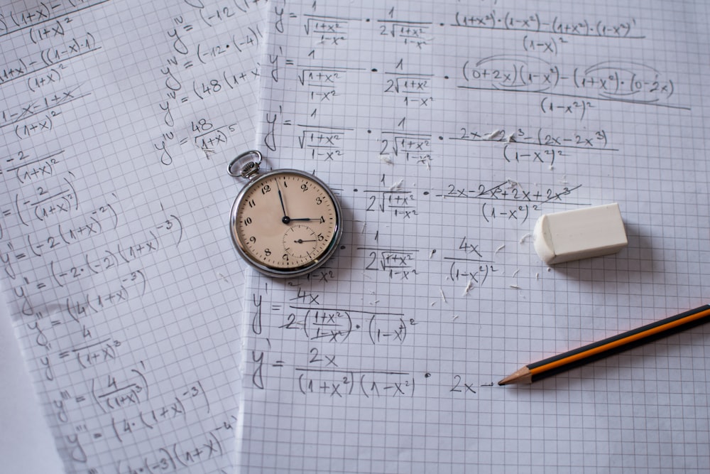 silver and white round analog watch beside white printer paper